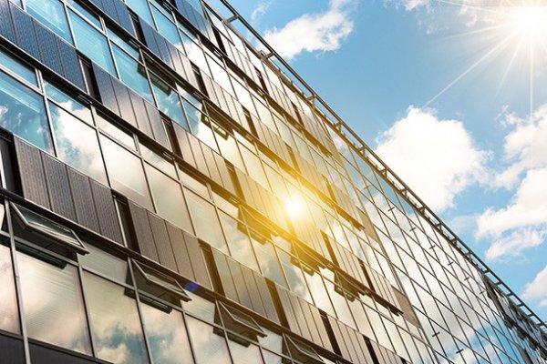 The sun shines on solar panels attached to a glass building.