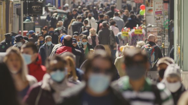 Anonymous crowd of people walking along a street wearing masks