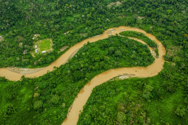 Aerial view of a brown river winding through rainforest with a village nearby