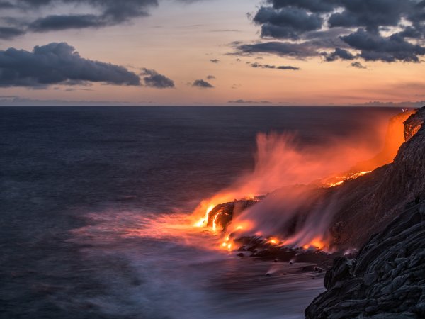 Lava pours into the ocean creating steam at sunset