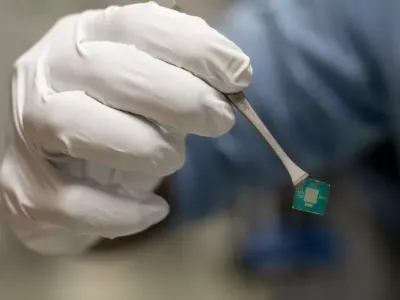 A gloved hand holds a microchip with tweezers