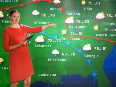 A woman in a red dress stands in front of a weather map and points