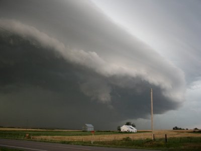 A large storm cloud over a farmhouse and flat fields