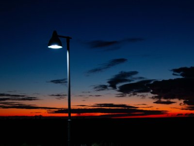 A streetlamp shines light with a sunset in the background