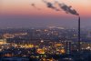 Smoke emits from a smokestack with a city skyline at sunset